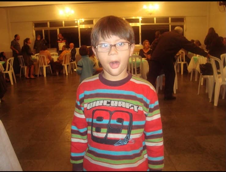 Kevin criança, de óculos e blusa listrada, fazendo careta numa festa