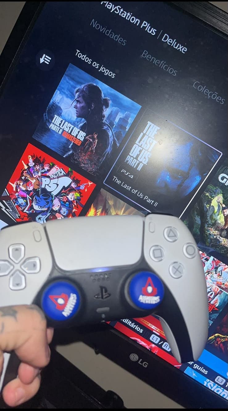 Controle de PlayStation em frente à TV com a biblioteca de jogos aberta