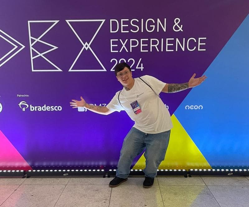 Kevin no Design & Experience 2024, de braços abertos em frente ao painel do evento